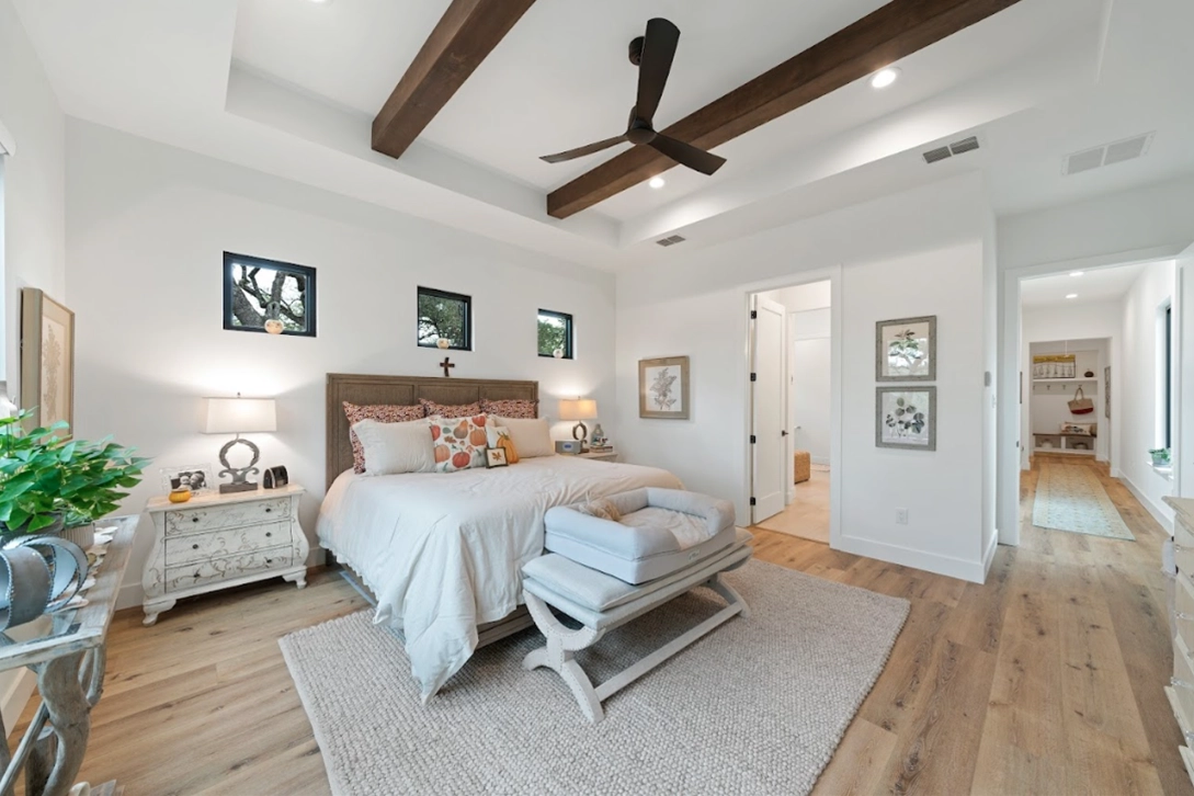 Peaceful bedroom with wooden flooring, a high ceiling with exposed wooden beams, a large bed, soft lighting, and natural light from windows.