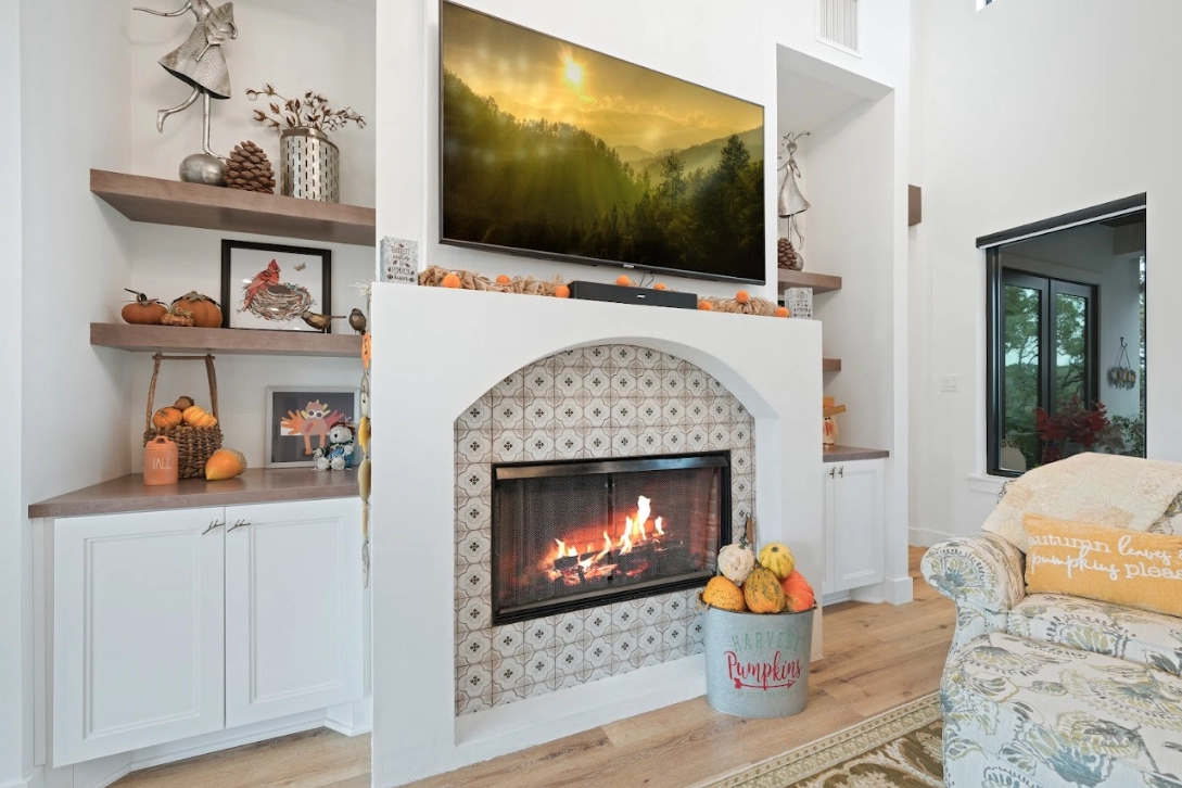 Cozy living room corner featuring a charming fireplace with decorative tiles, built-in shelves with seasonal decor, and a mounted television.